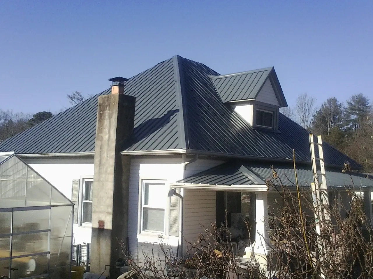 Dark blue standing seam metal roof on a white farmhouse with dormer — Slate & Tile Roof Repair by Roofing Brothers in Saint Francis