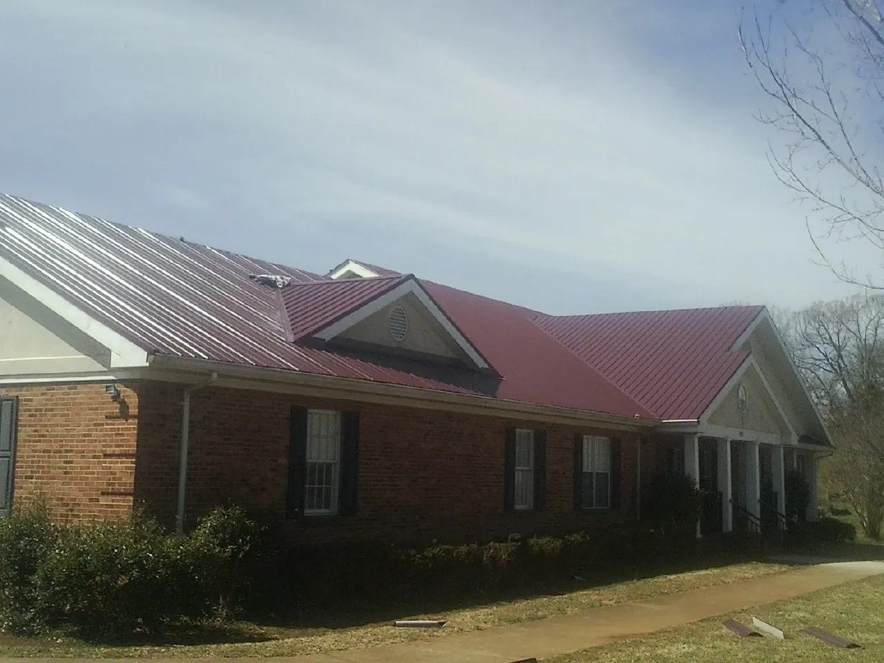 Red metal roof with gabled entries on a long brick building, from a Hail Damage Roof Repair job in Saint Francis
