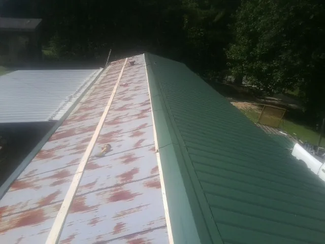 Old rusted panels beside newly installed green metal roofing — Wind Damage Roof Repair by Roofing Brothers in Saint Francis